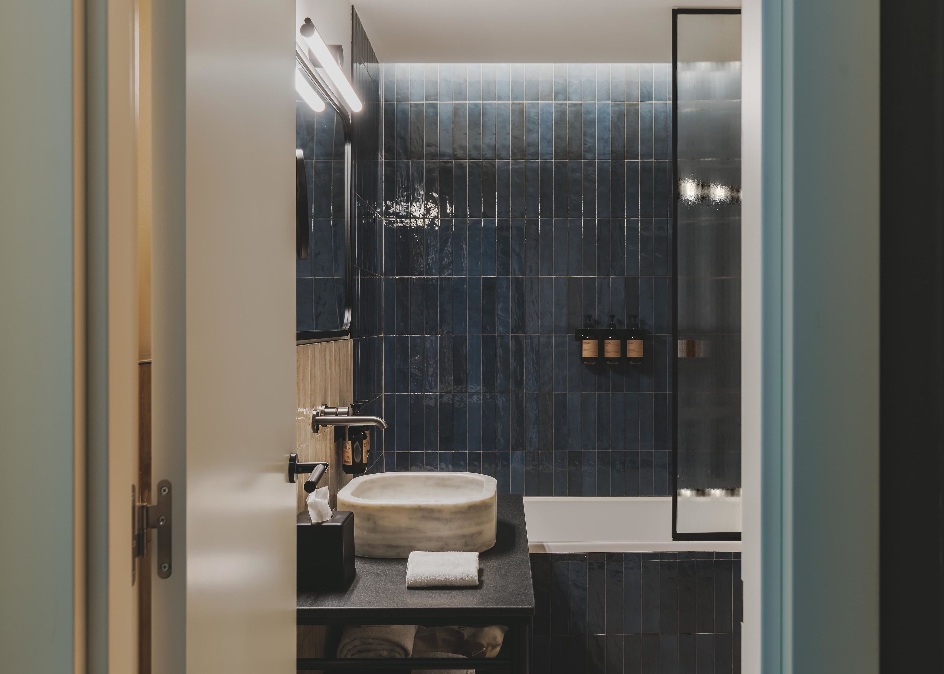 A bathroom with dark blue tiles, a round sink, and a mirror.