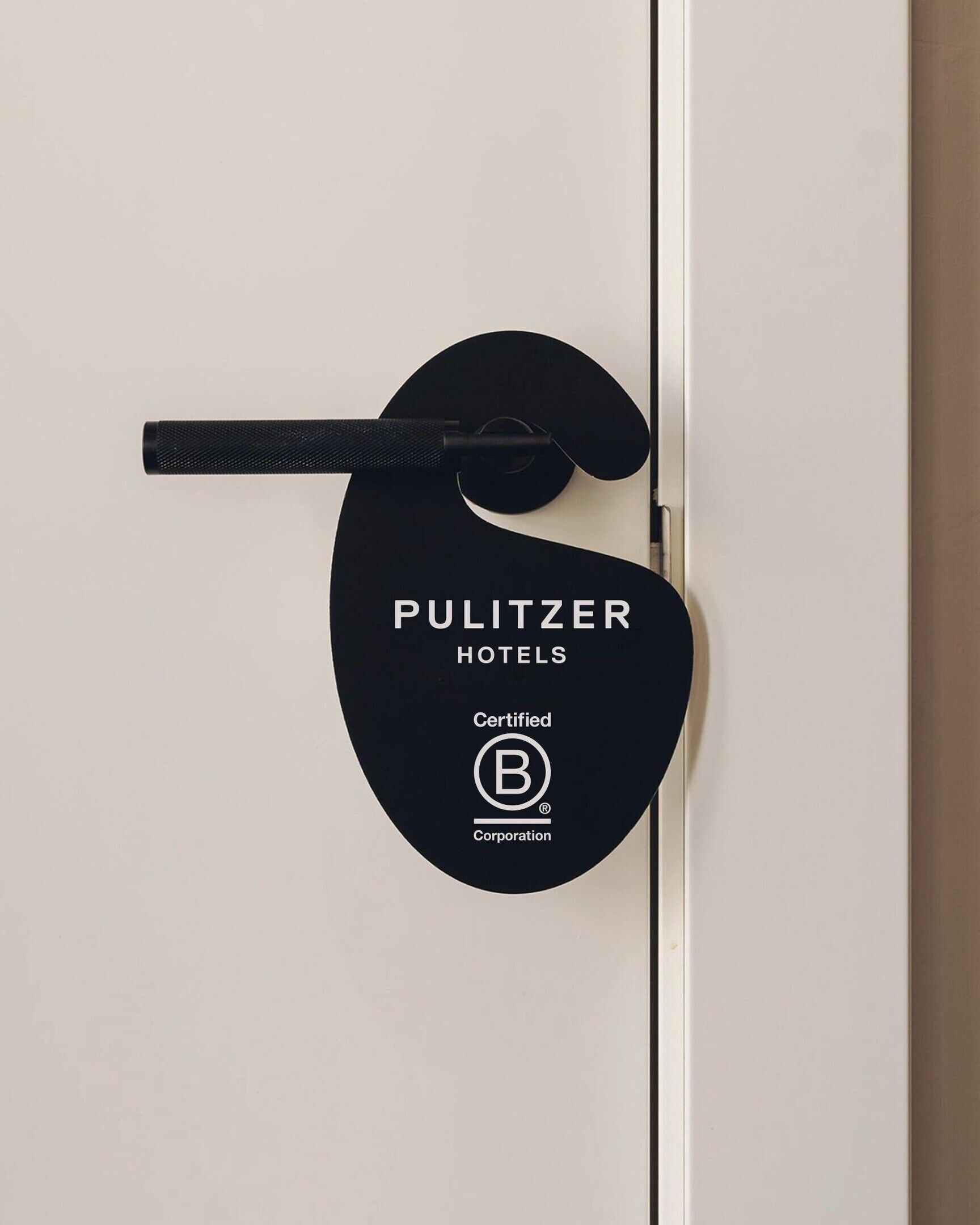 Una puerta con un letrero negro que indica 'PULITZER HOTELS' y el logotipo de 'Certified B Corporation'.