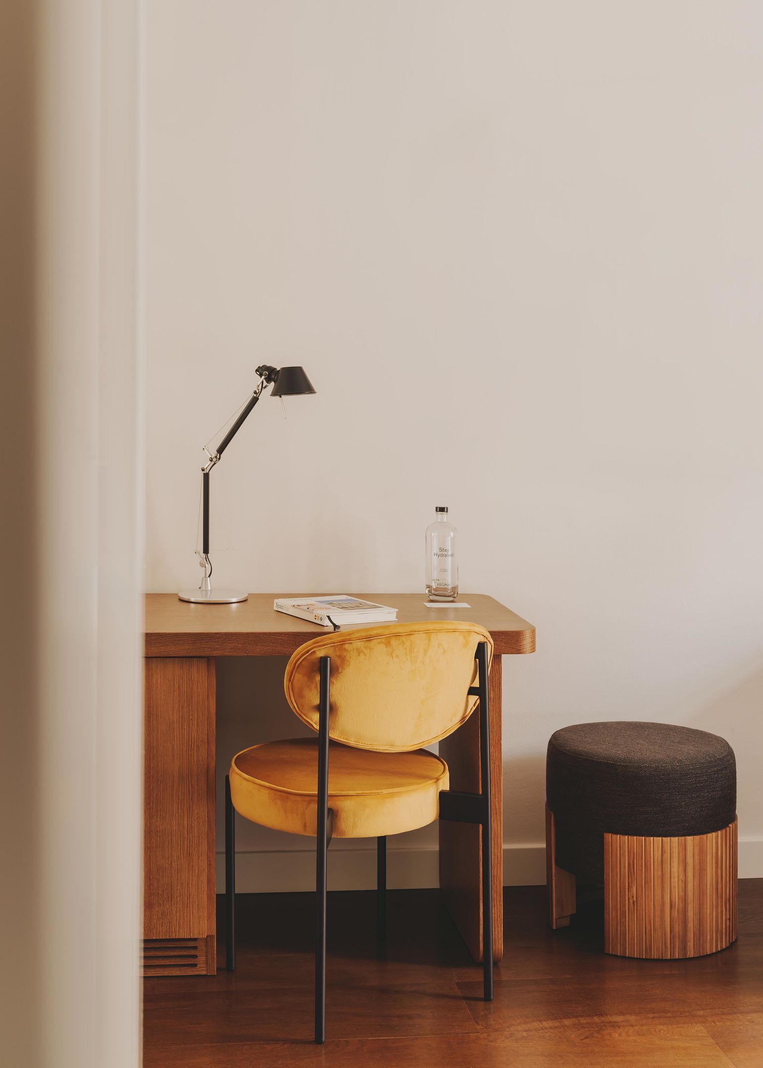 Uma mesa de madeira com uma cadeira amarela, uma luminária de mesa preta e uma garrafa de água.