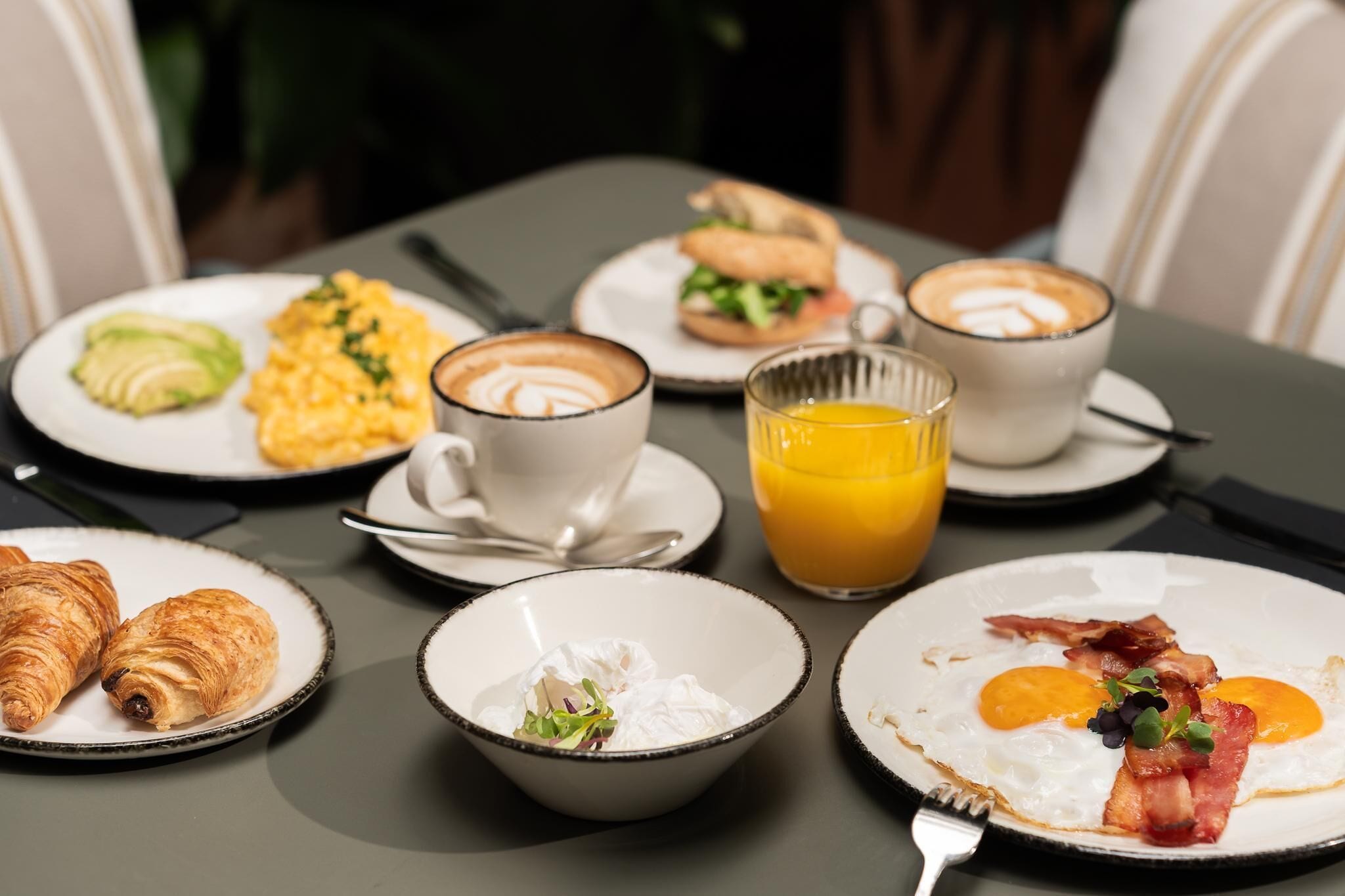 Mesa de café da manhã com croissants, ovos mexidos, bacon e café.