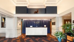 A reception area with a marble counter, a sign reading "VOCO AN IHG HOTEL," and a deer sculpture on the ceiling. - voco Edinburgh - Royal Terrace by IHG (Edinburgh)