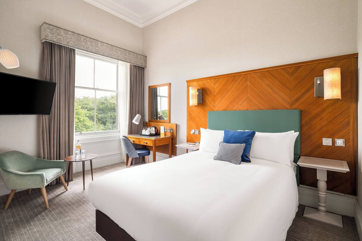 A hotel room with a large bed, a desk, a chair, a television, and a window with curtains.