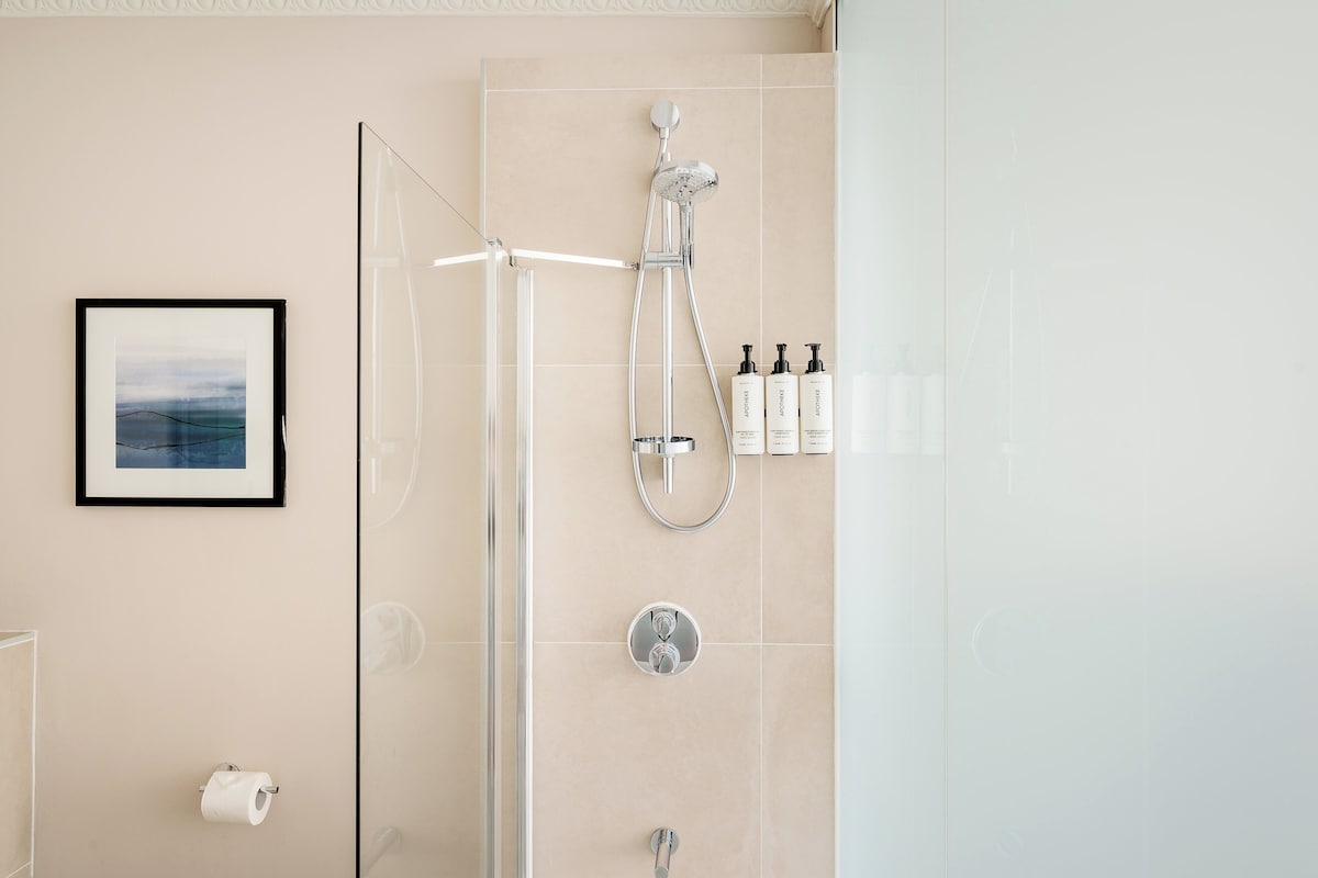 Un baño moderno con cabina de ducha de vidrio, un cuadro enmarcado en la pared y artículos de aseo en un estante.