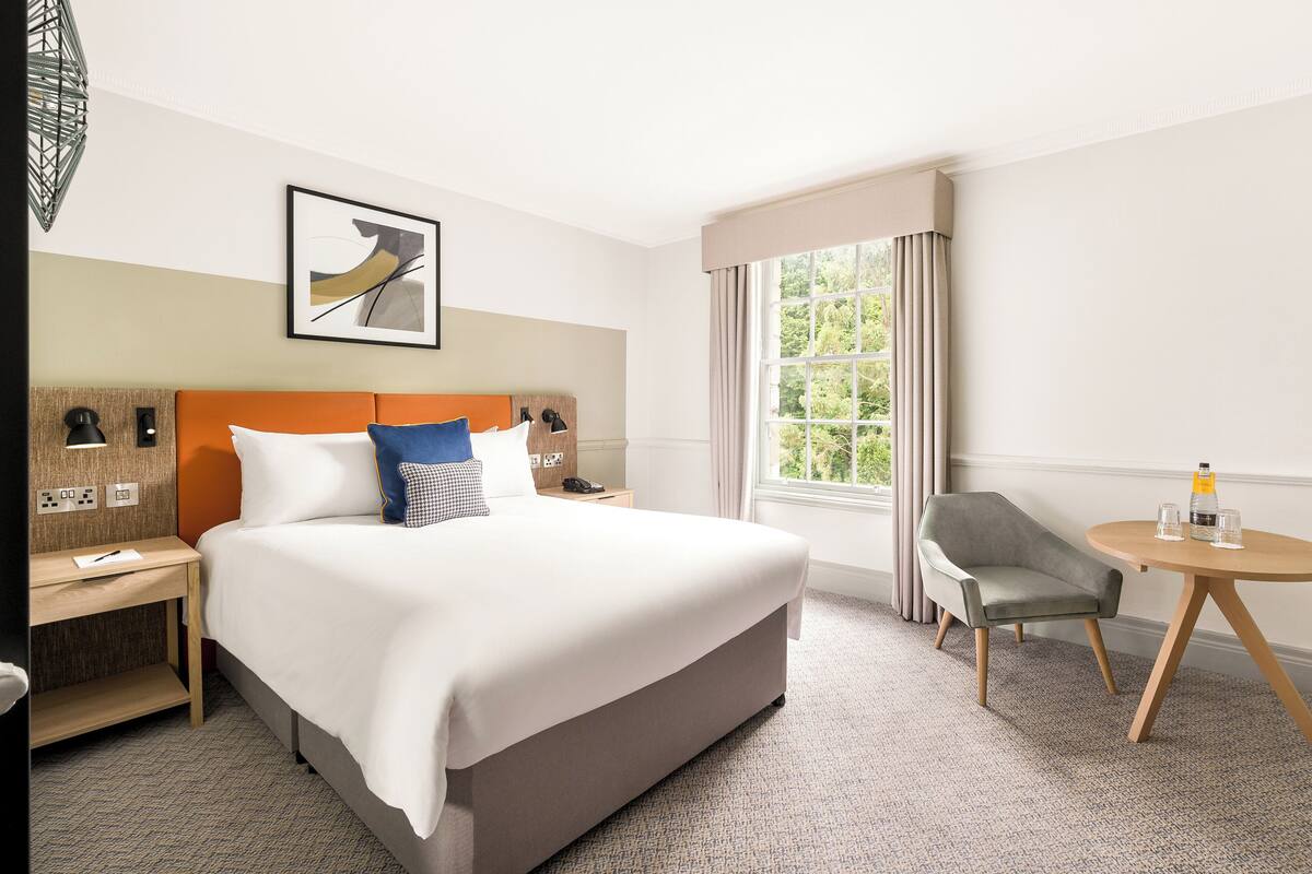A hotel room with a bed, a desk, a chair, a round table, and a window with curtains.