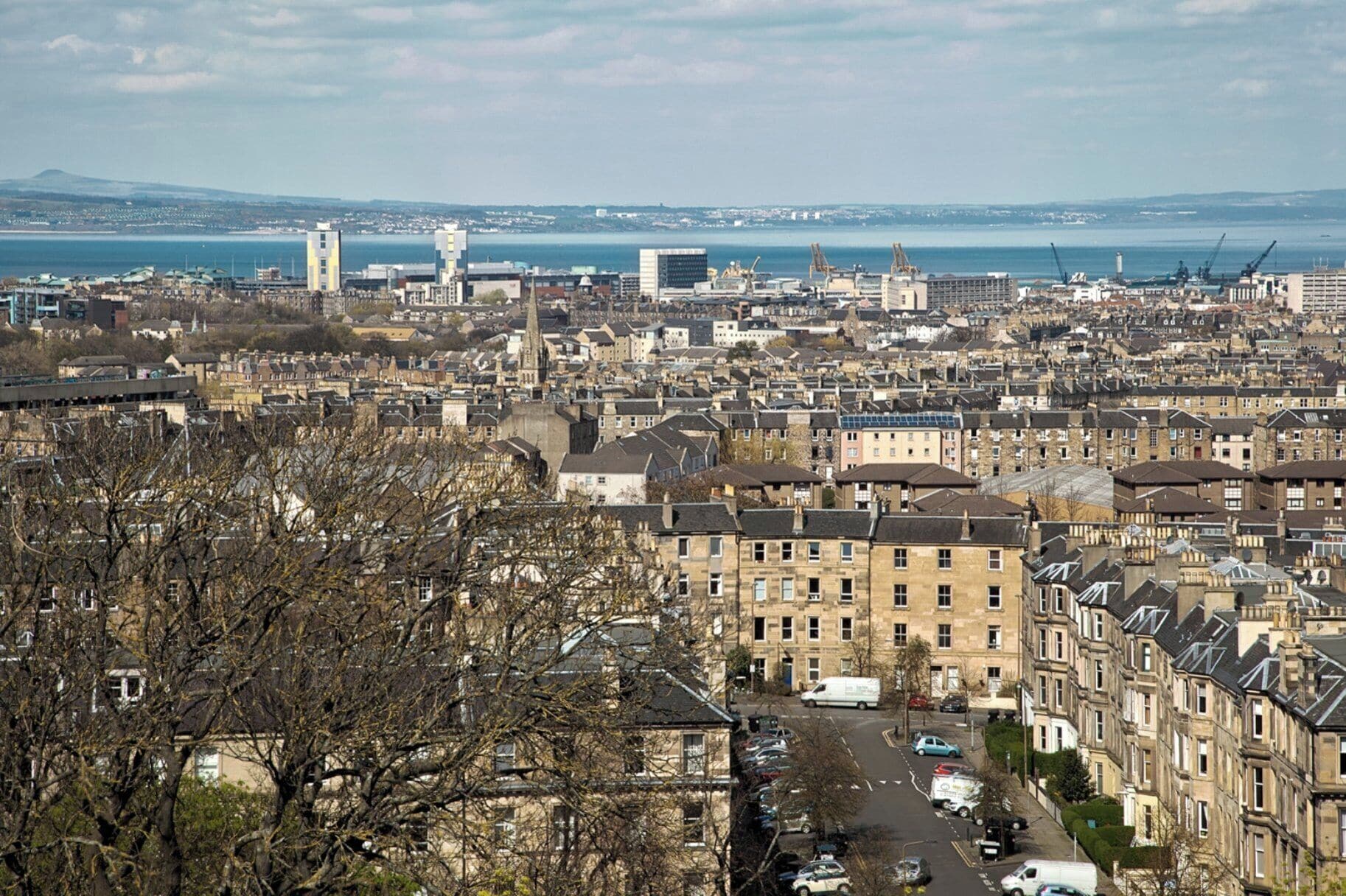 A cityscape with residential buildings, a clear sky, and a body of water in the distance.