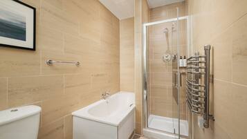 A modern bathroom with a bathtub, toilet, and glass shower enclosure.