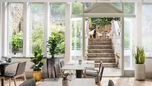 A bright dining area with large windows, potted plants, and a view of a stone staircase leading outside. - voco Edinburgh - Royal Terrace by IHG (Edinburgh)