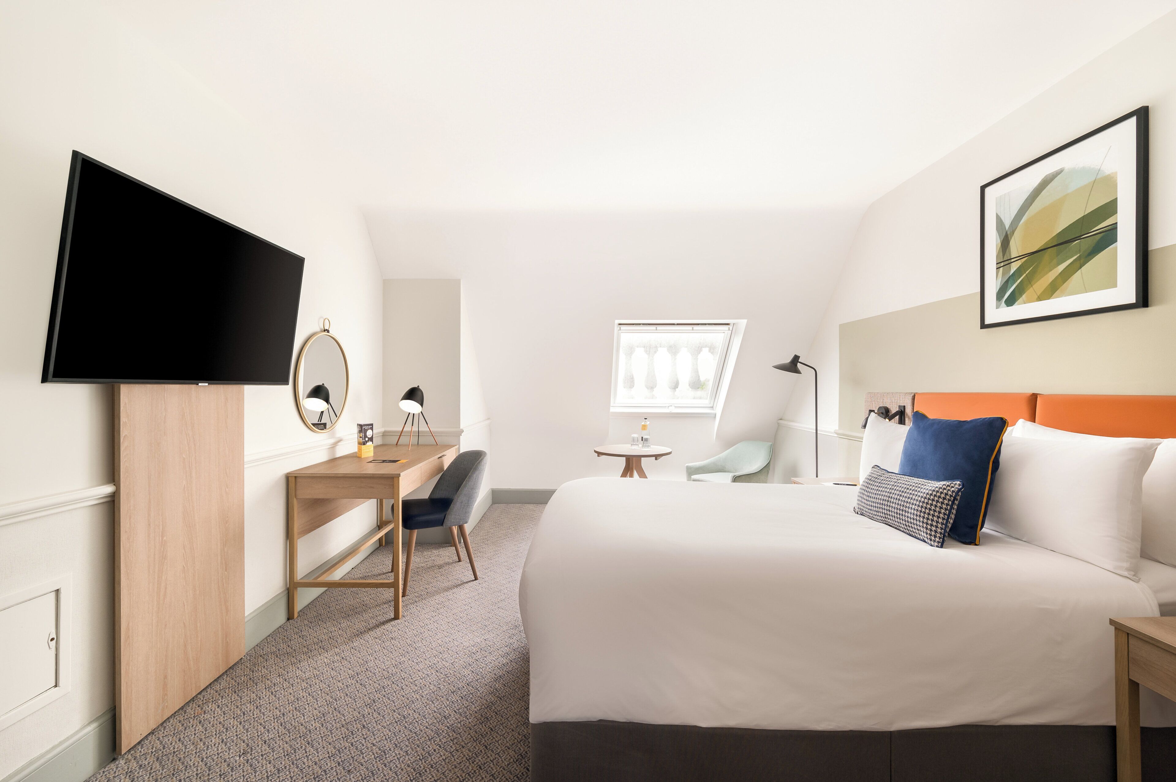 Hotellihuone, jossa on sänky, työpöytä, tuoli, televisio ja ikkuna.