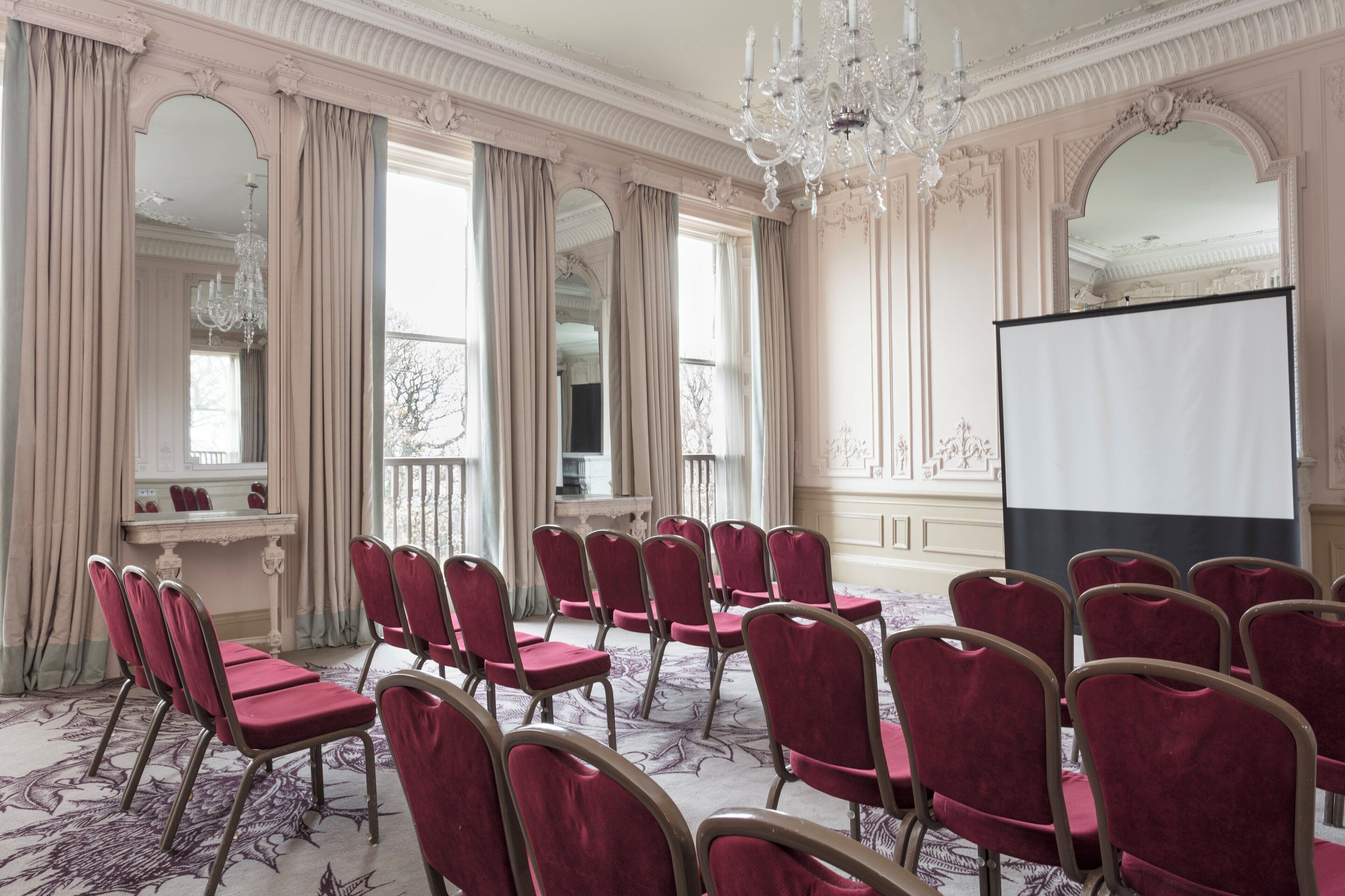 A conference room with a whiteboard, multiple rows of red upholstered chairs, and a chandelier.
