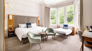 A hotel room with a large bed, two armchairs, a small table, and a window with curtains. - voco Edinburgh - Royal Terrace by IHG (Edinburgh)