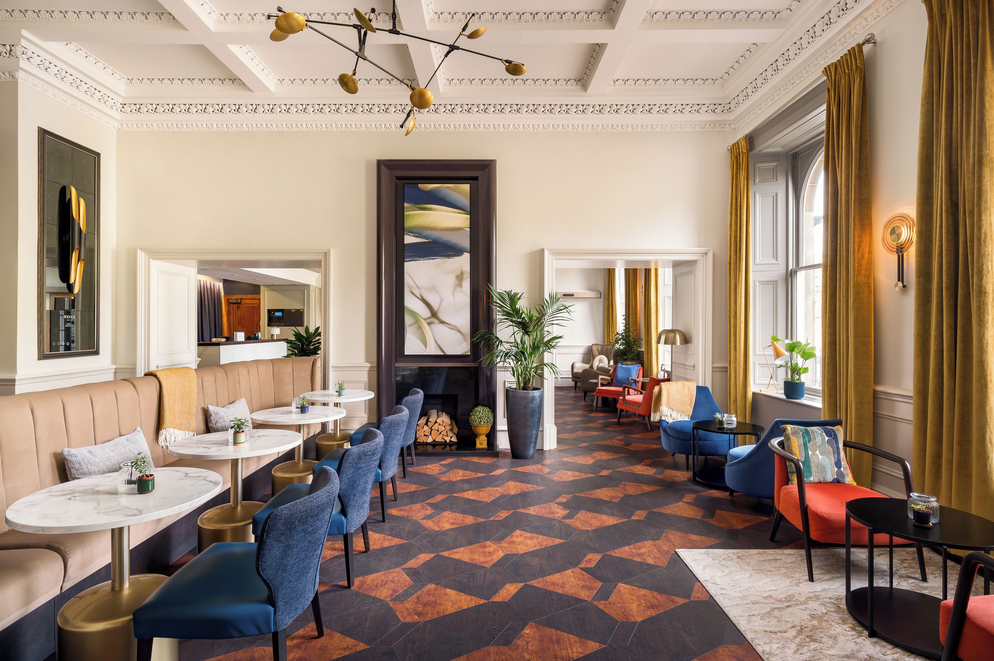 A hotel lobby with a central fireplace, seating areas, and a patterned floor.
