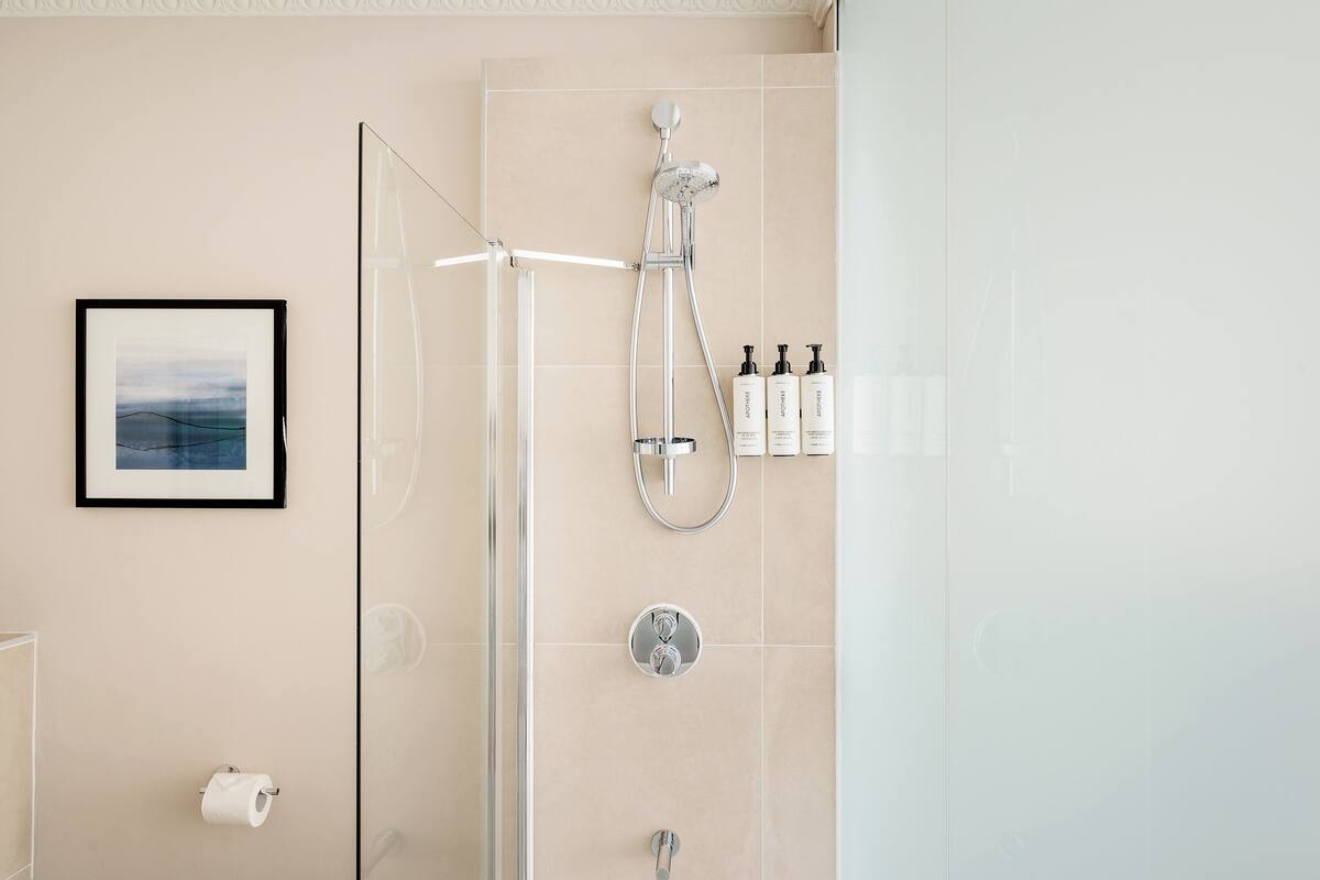 A modern bathroom with a glass shower enclosure, a framed picture on the wall, and toiletries on a shelf.