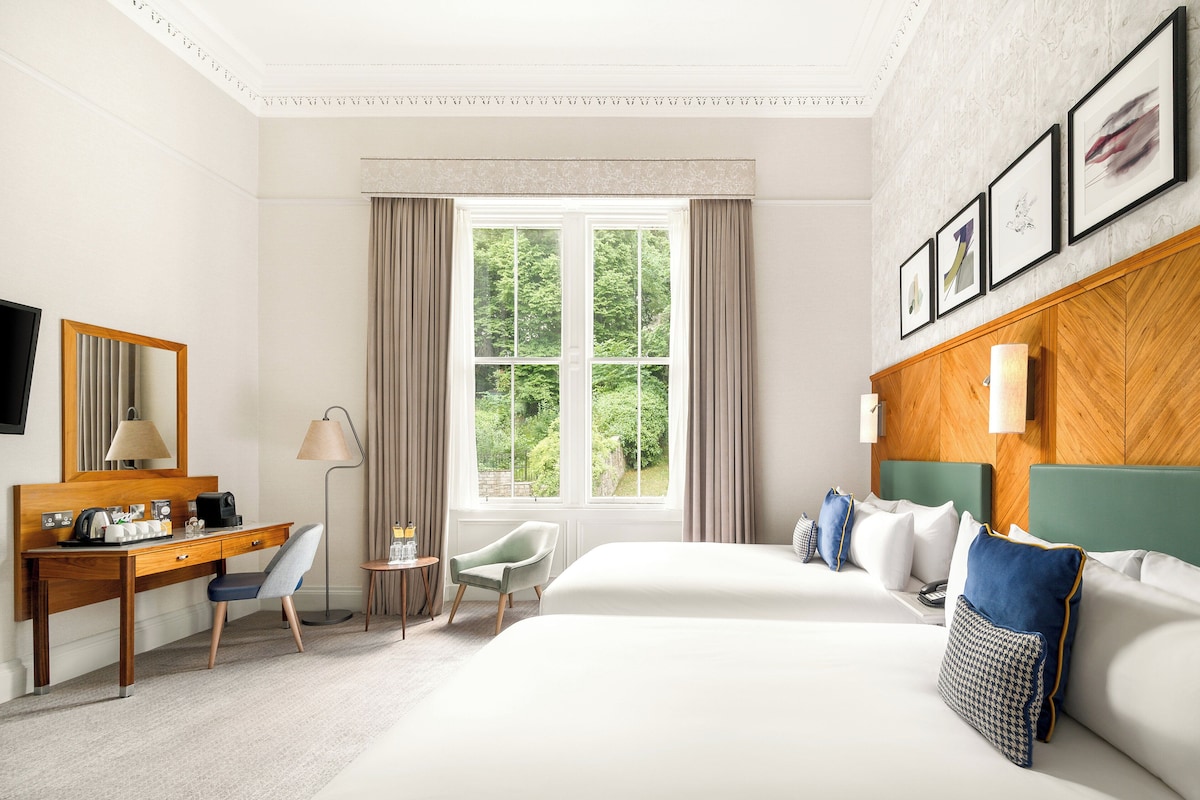 A hotel room with a large bed, a desk, a chair, a television, and a window with curtains.