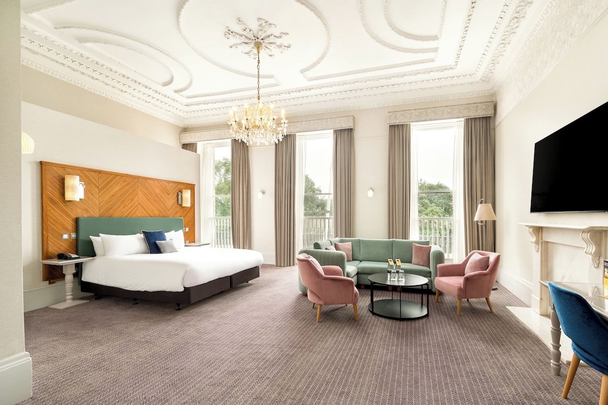 A hotel room with a large bed, a green sofa, a round coffee table, and a TV.