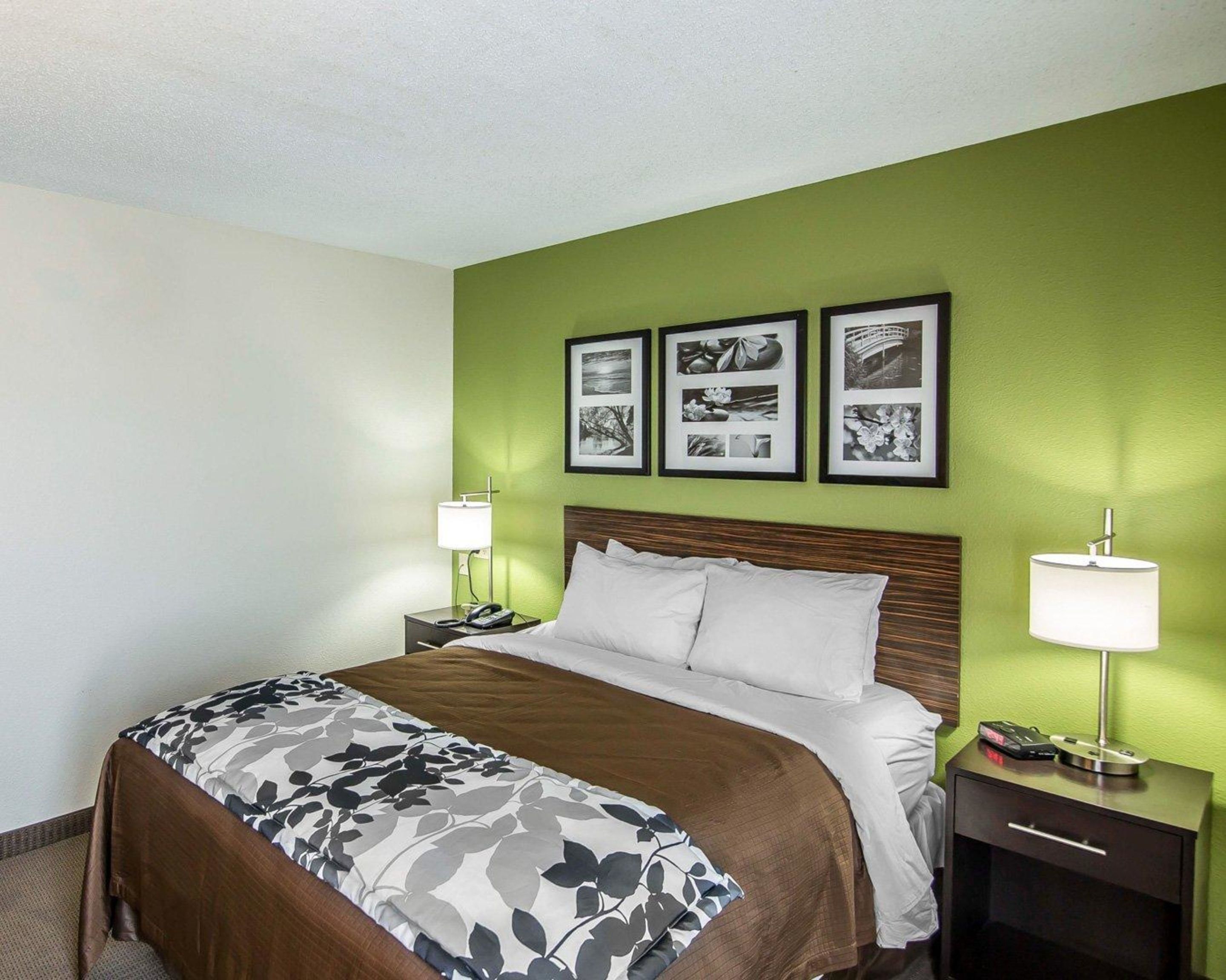 A hotel room with a bed, two bedside tables, a nightstand, a lamp, and three framed pictures on the wall.