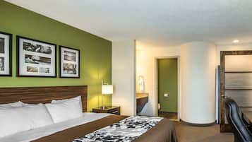 Una habitación de hotel con cama, mesita de noche, lámpara, silla y puerta de baño.