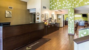 A hotel reception area with a dark wooden reception desk, a clock, and a wall-mounted sign that reads "Sleep Inn".