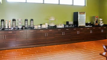 Un long comptoir avec différents types de machines à café et une variété de produits alimentaires, un meuble avec des tiroirs et une fenêtre au-dessus.