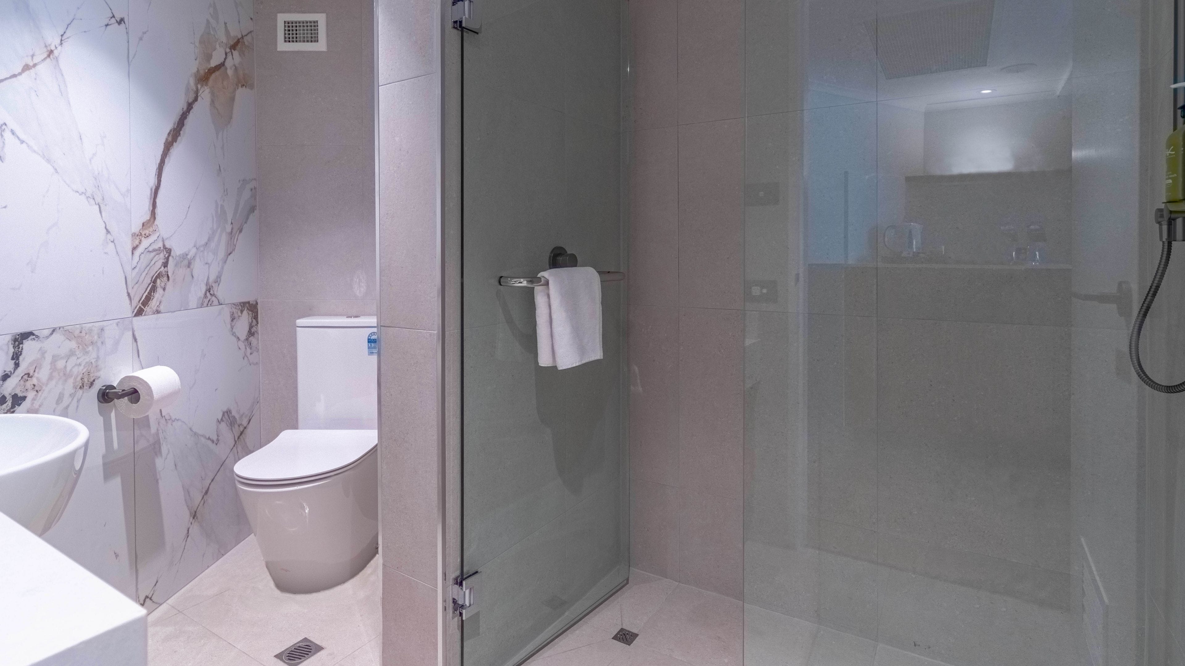 A modern bathroom with a marble wall, a toilet, a glass shower enclosure, and a sink.