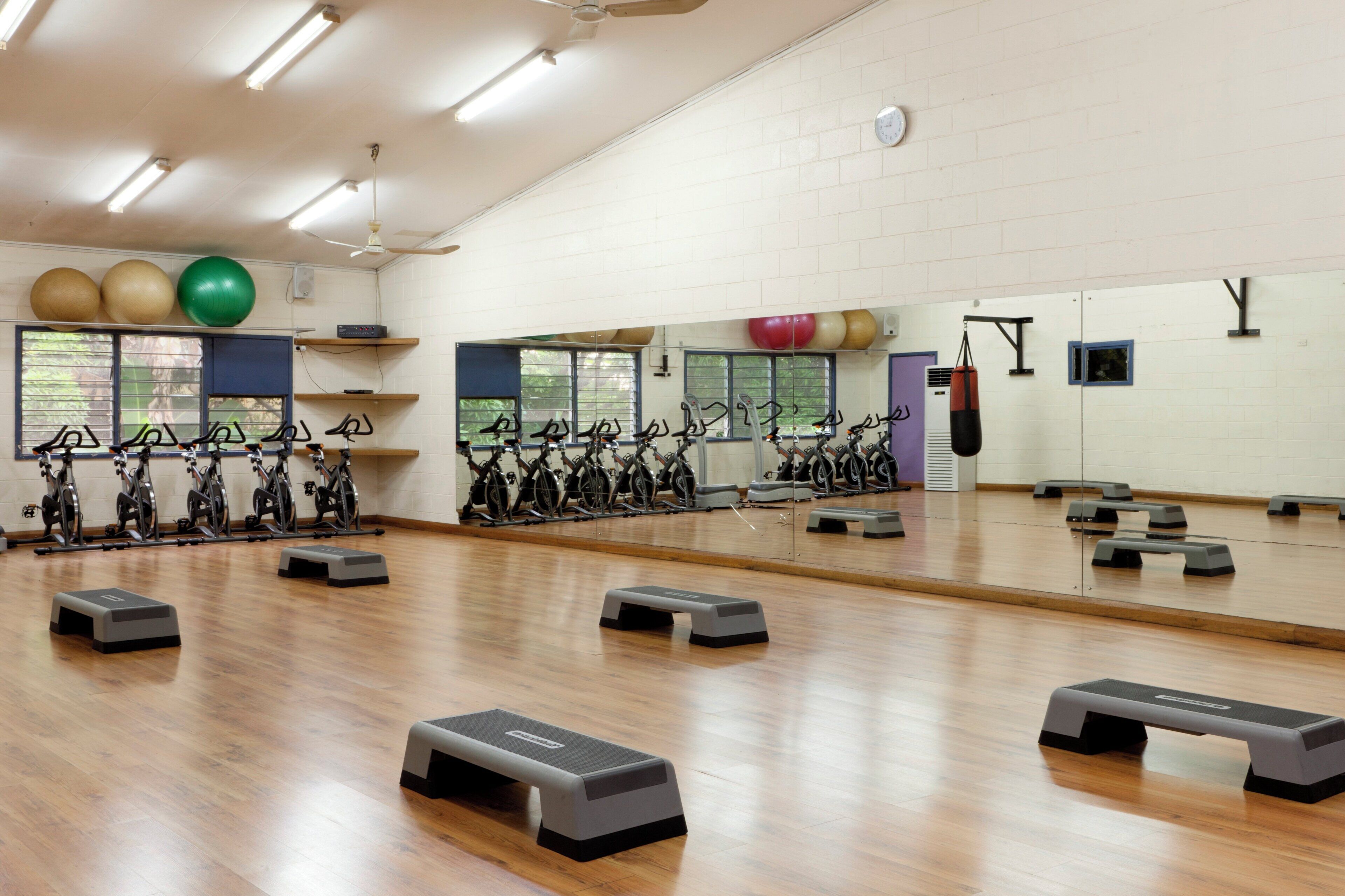 A gym with exercise equipment, a large mirror, and wooden flooring.