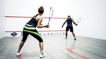 To personer spiller squash i et rum med trægulv og en hvid væg med røde linjer.