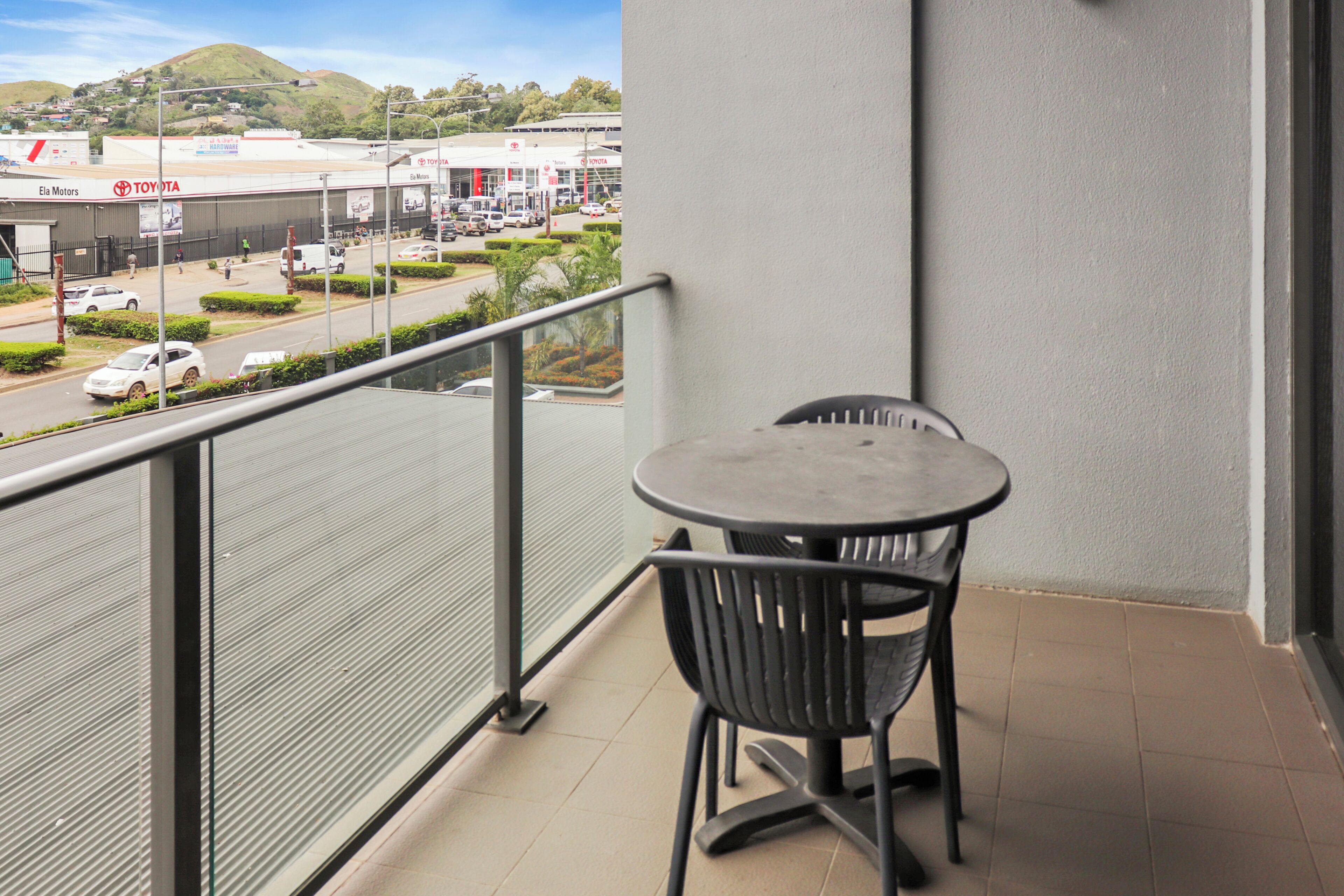Een balkon met een tafel en stoelen, met uitzicht op een straat met auto's en een gebouw met een Toyota-bord.