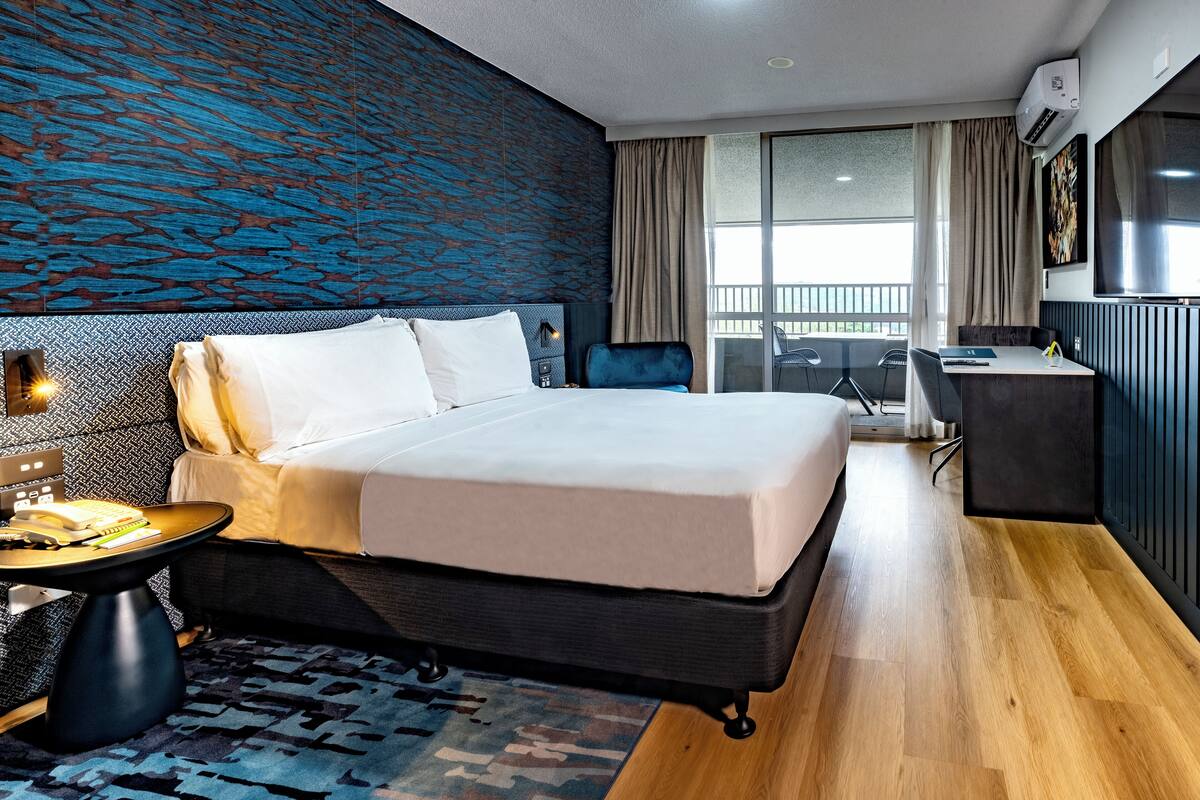 A modern hotel room with a large bed, a desk, and a view of the outdoors.