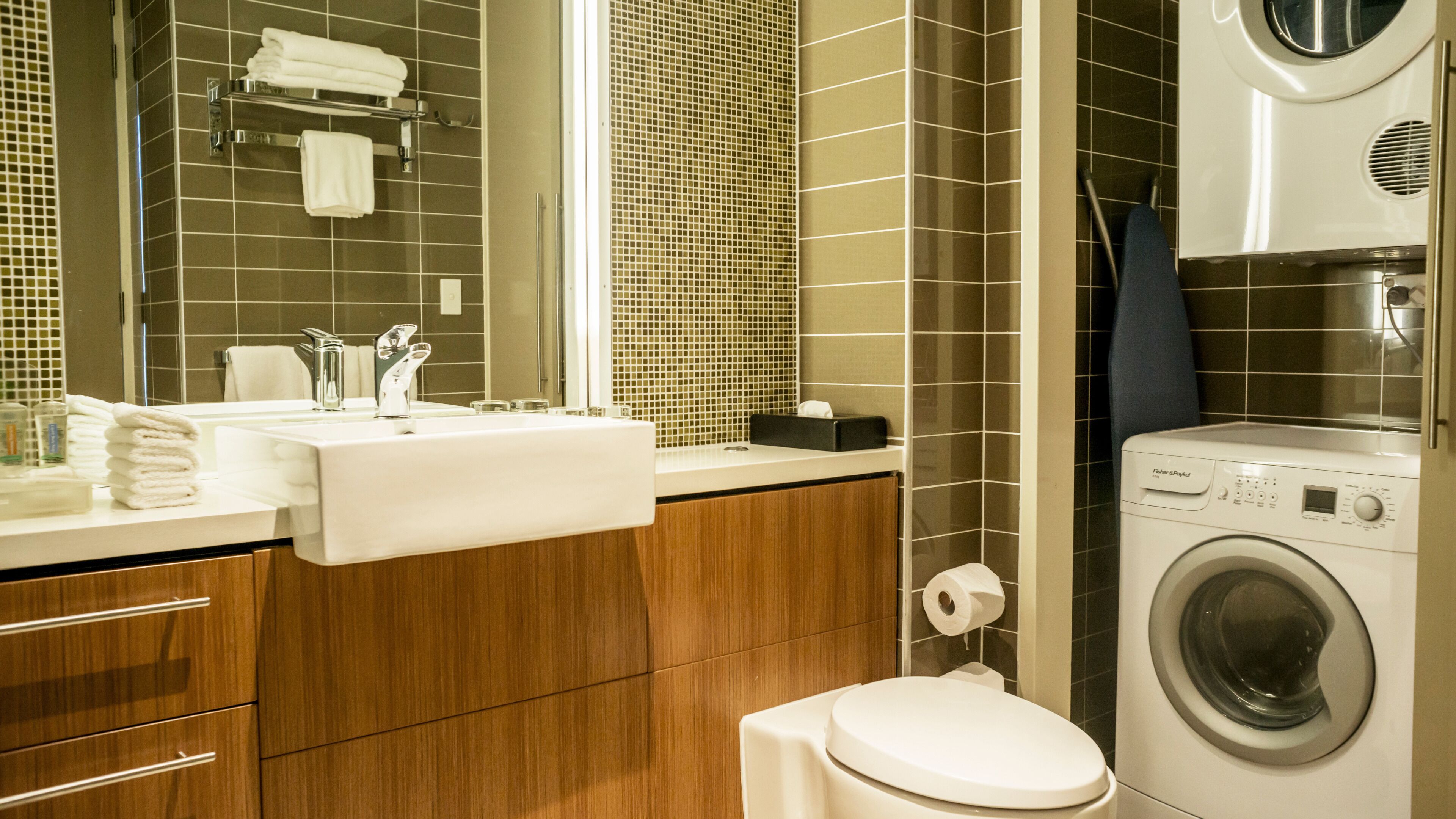 A modern bathroom with a sink, mirror, towel rack, toilet, and a washing machine.