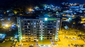 A multi-story Holiday Inn & Suites building with a central courtyard, parking area, and surrounding residential area at night. - Holiday Inn Port Moresby by IHG (Port Moresby)