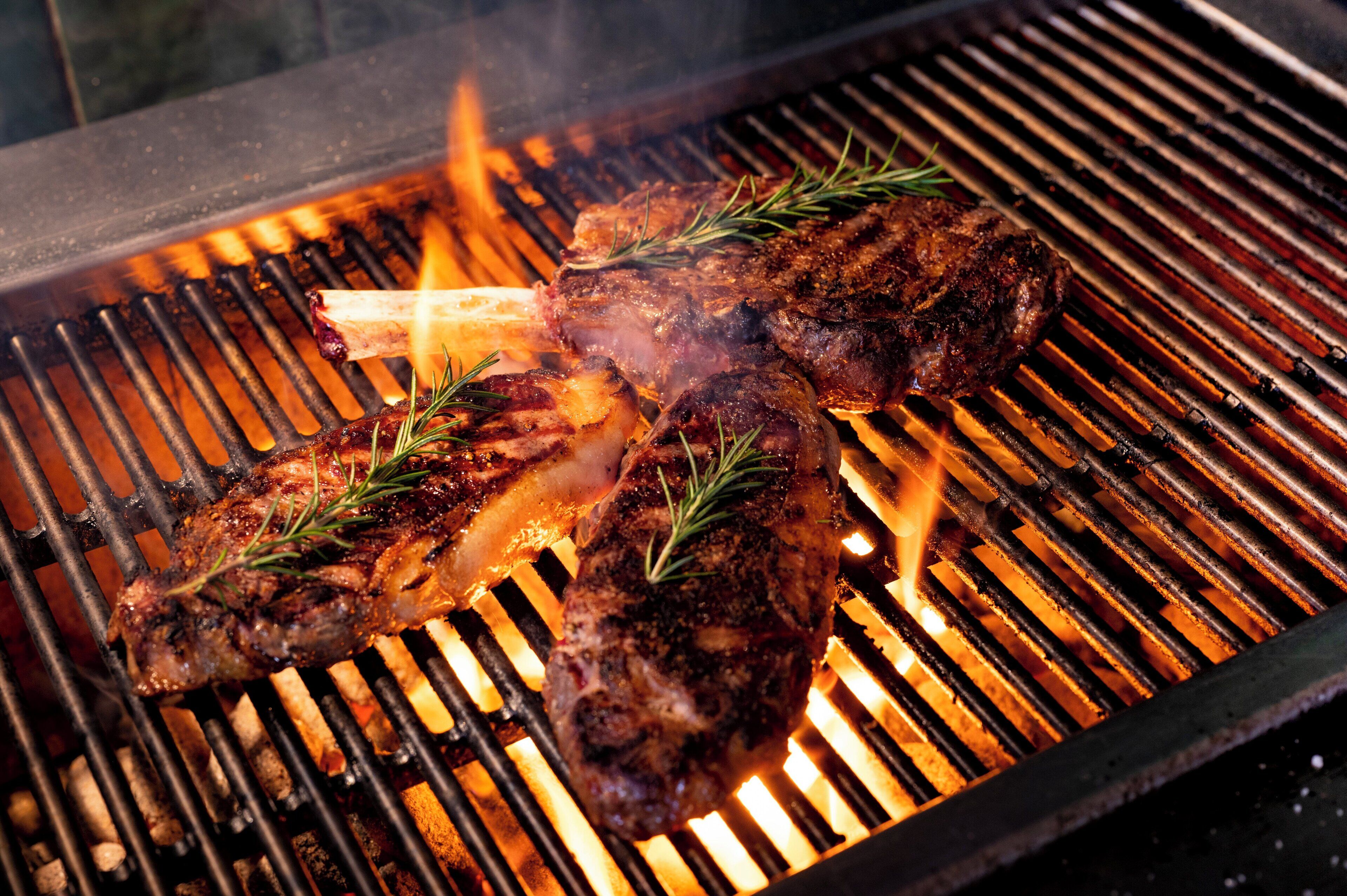 Un filete asándose en una barbacoa con llamas visibles y ramitas de romero.