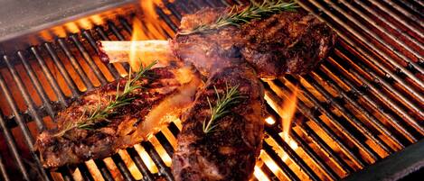 Un filete asándose en una barbacoa con llamas visibles y ramitas de romero.