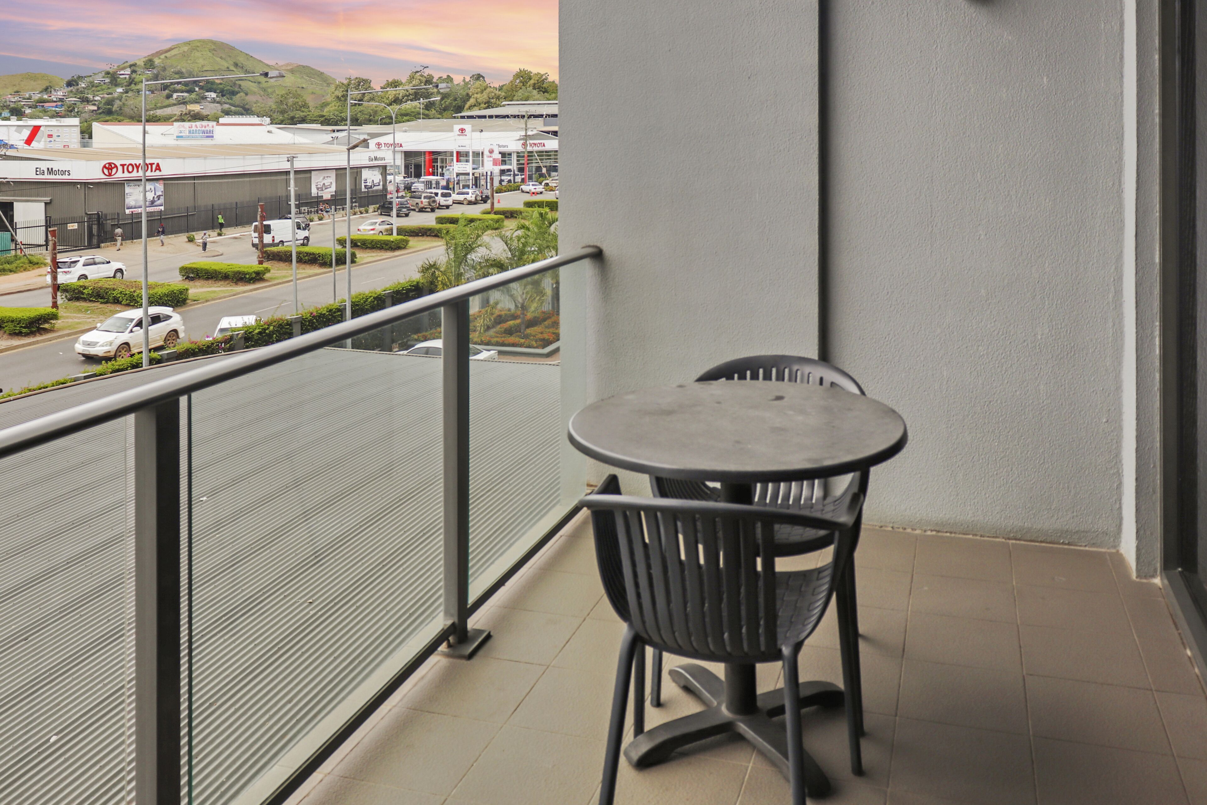 Ein Balkon mit Tisch und Stühlen, mit Blick auf eine Straße, im Hintergrund ein Toyota Autohaus.
