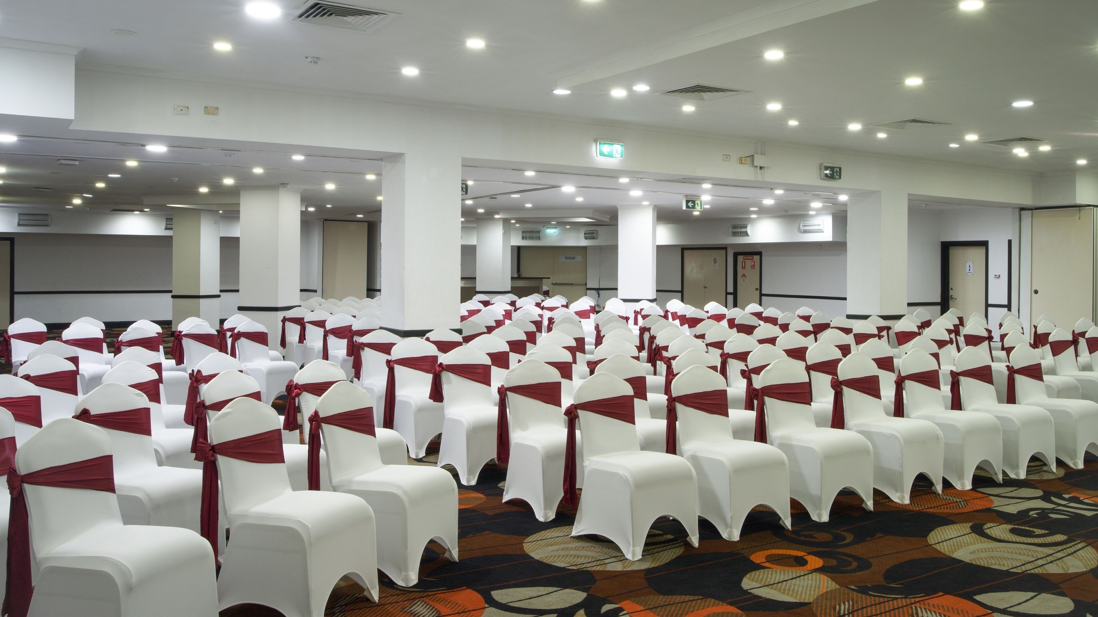 A conference room with rows of white chairs, each with a red sash, and a patterned carpet.