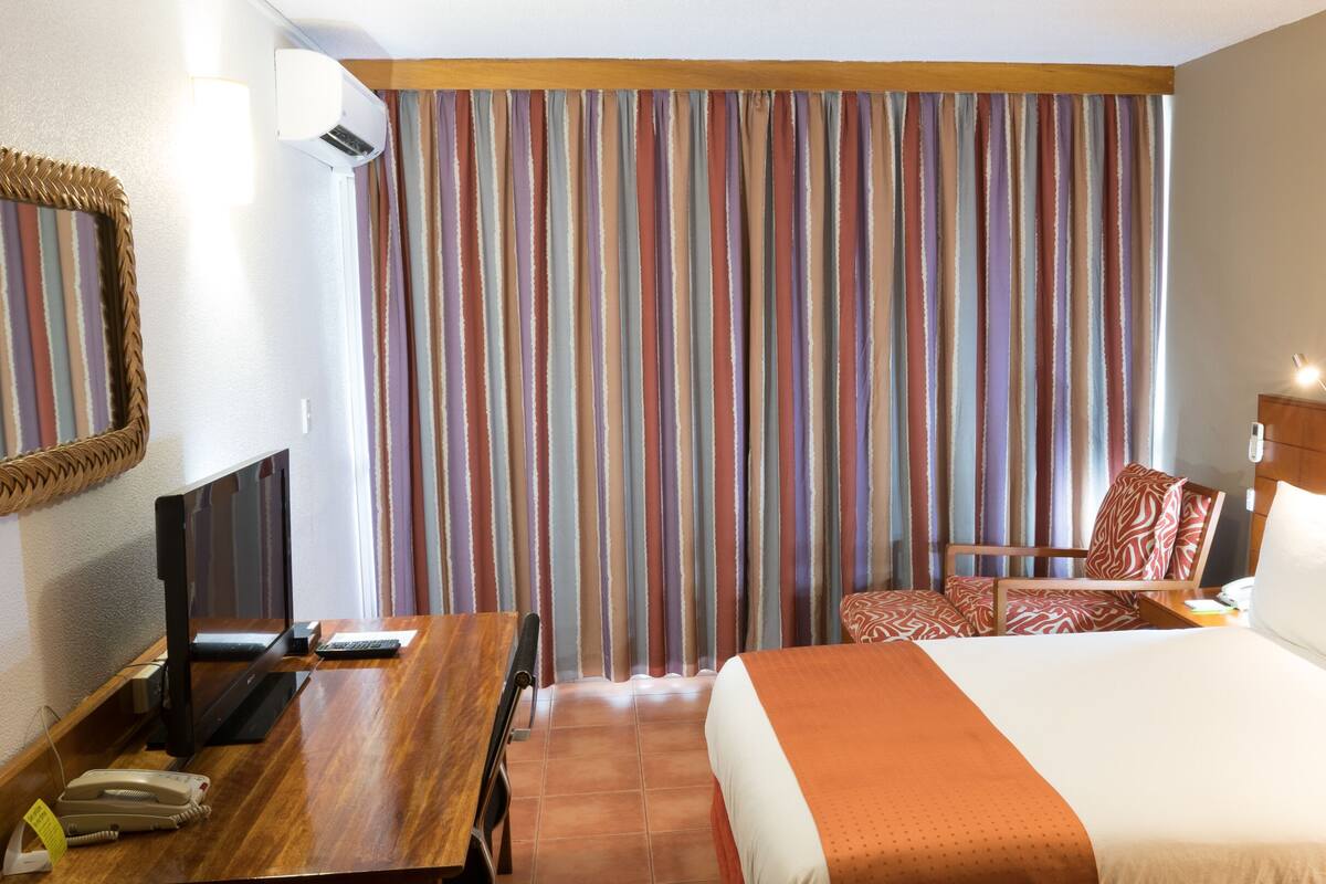 A hotel room with a bed, a desk with a telephone, a chair, and a television.