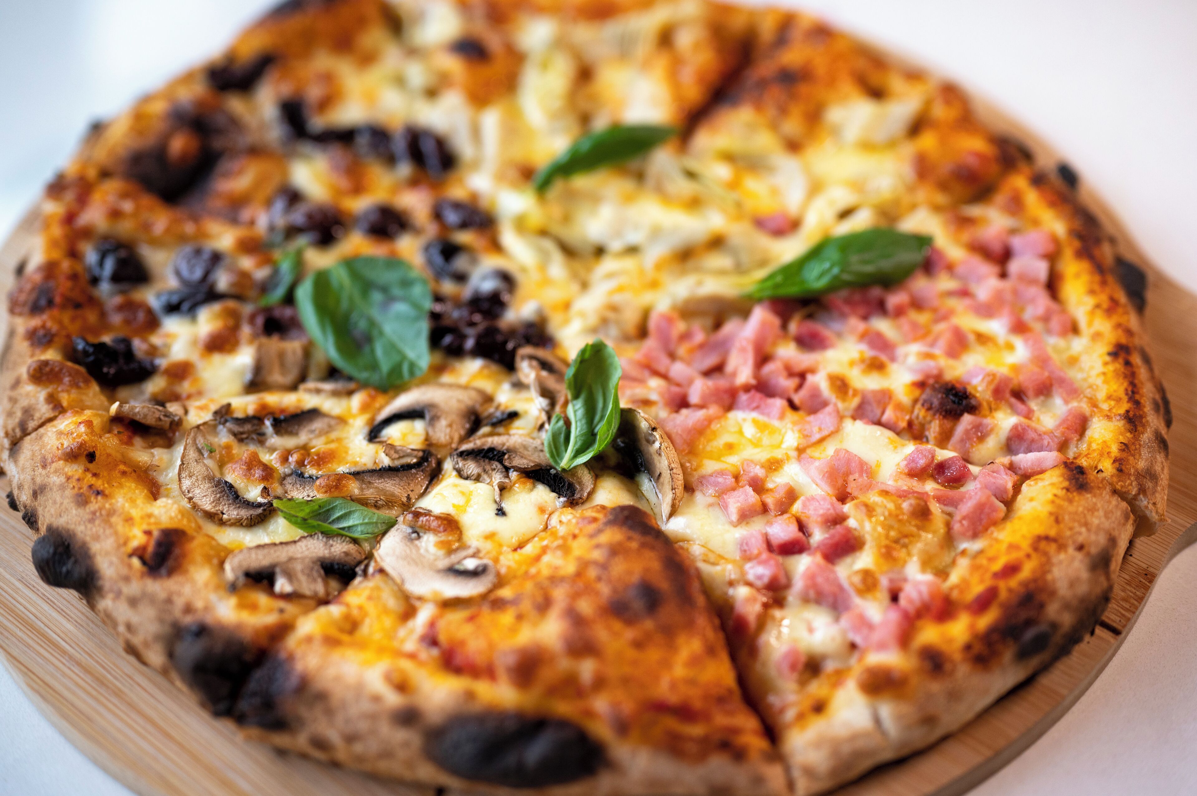 A pizza with various toppings, including mushrooms, ham, and spinach, on a wooden board.
