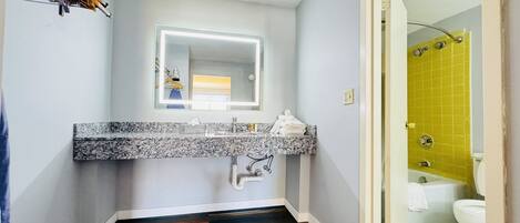 A bathroom with a marble countertop, a mirror, and a shower with yellow tiles.