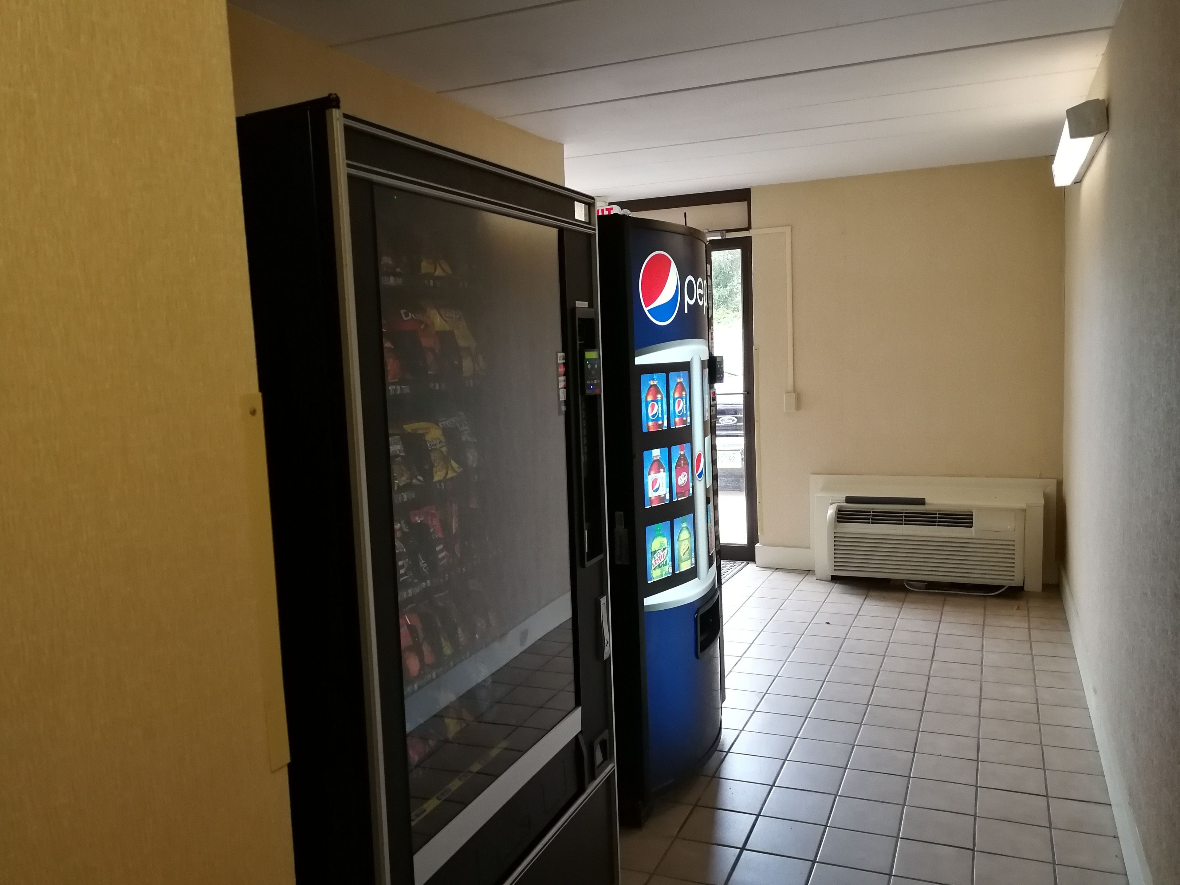 Máquina expendedora con el logo de Pepsi, un refrigerador y un aire acondicionado montado en la pared en un pasillo.