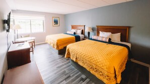 A hotel room with two beds, a desk, and a window.
