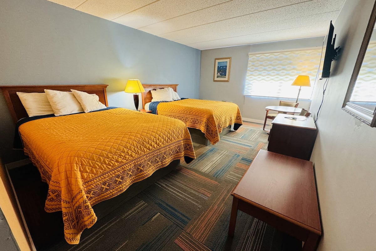 A hotel room with two beds, a desk, a chair, a TV, and a window with a view.