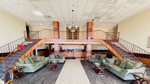 A spacious lobby with a central seating area, a kitchen in the background, and a staircase connecting two floors.