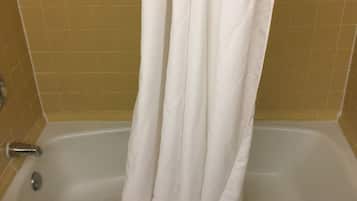 Una bañera con una cortina blanca, una toalla blanca y una pequeña botella de champú en el borde.
