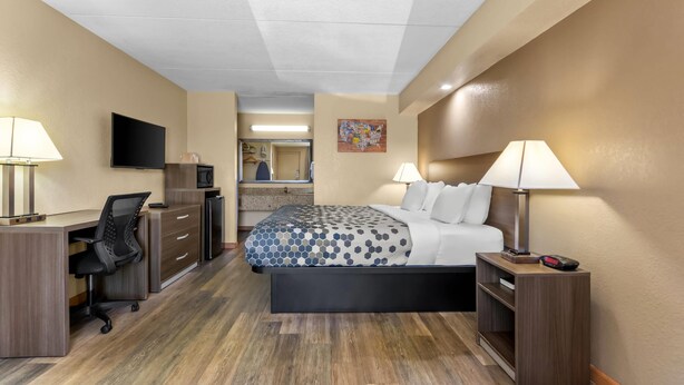 Una habitación de hotel con cama, escritorio, silla, televisión y una pequeña kitchenette.