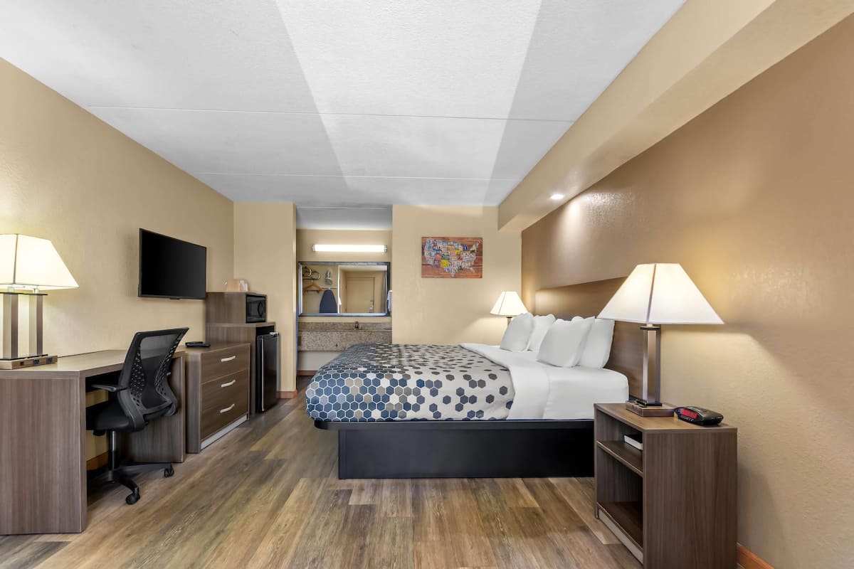 Una habitación de hotel con cama, escritorio, silla, televisión y una pequeña kitchenette.