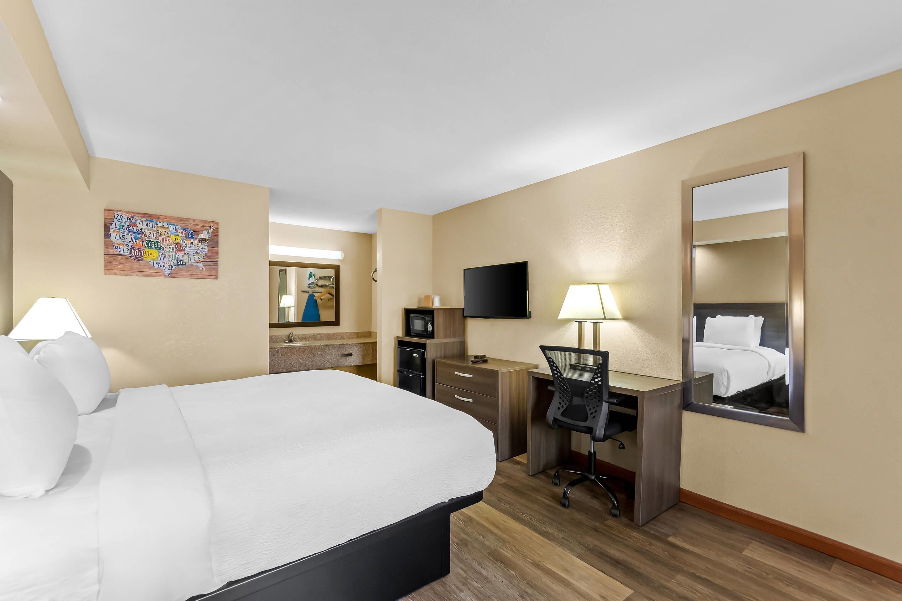A hotel room with a large bed, a desk with a chair, a TV, a mirror, and a map on the wall.