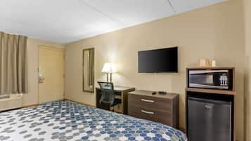 Ett hotellrum med en säng, ett skrivbord, en tv, en mikrovågsugn och ett kylskåp.
