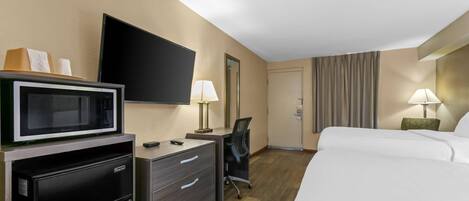 A hotel room with a bed, a desk with a computer, a microwave, a refrigerator, a flat-screen TV, and two lamps.