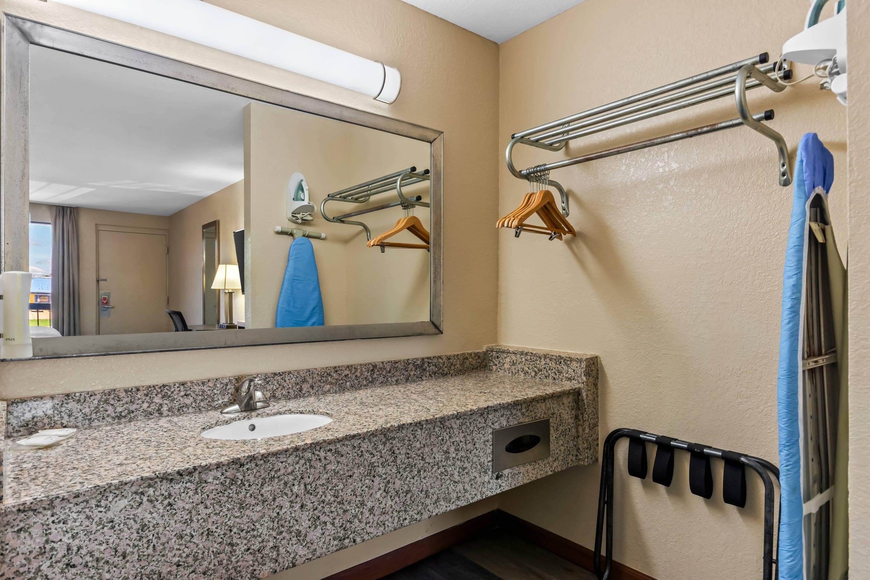 A bathroom with a granite countertop sink, a mirror, towel rack, and a towel rack with hangers.