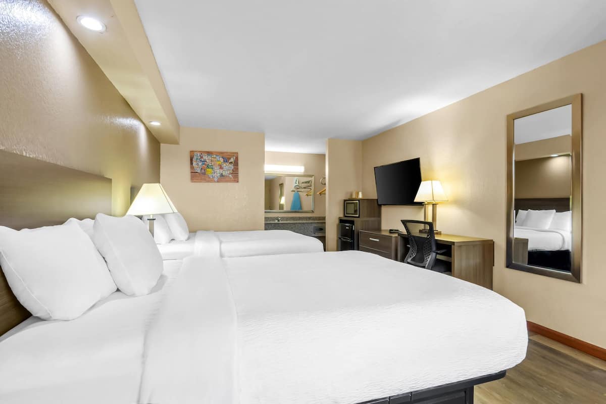 Habitación de hotel con dos camas, un escritorio, un televisor y un espejo.