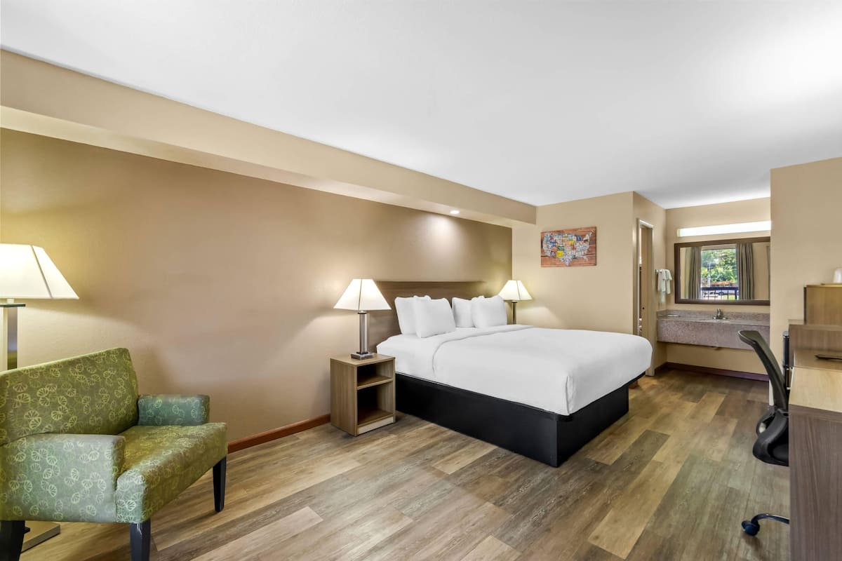 Una habitación de hotel con cama, una silla, un escritorio, una lámpara y una ventana.