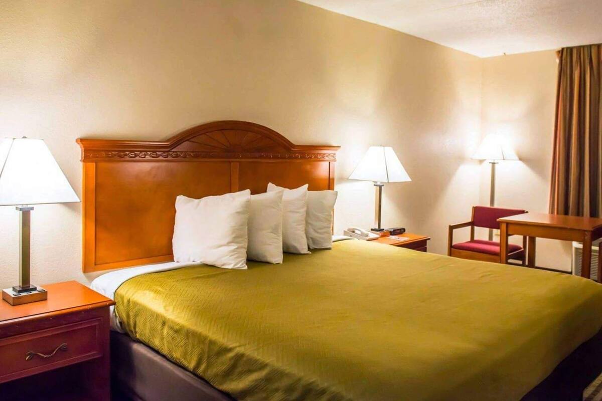 Una habitación de hotel con una cama, dos mesitas de noche, un escritorio y una silla.